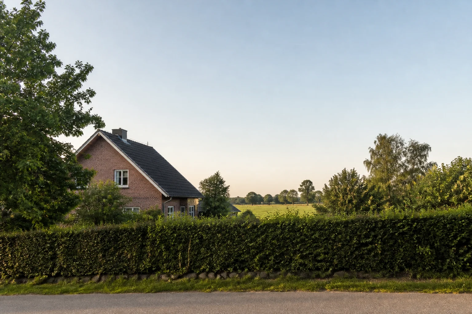 Ländlich geprägte Wohnlage mit Haus, Hecke und weitem Himmel